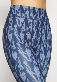 Vysoké legíny v modré barvě se strukturovaným abstraktním vzorem. Vyrobeny z pružného materiálu, mají ploché švy a hladký povrch.