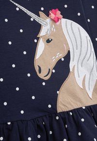 Navy-Kleid mit weißen Punkten, versehen mit einem bestickten Einhorn in Beige und Weiß, akzentuiert mit einer rosa Blume und einem silbernen Horn.