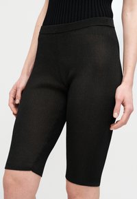 Μαύρα ραβδωτά ποδηλατικά σορτς με εφαρμοστή γραμμή, μήκος έως το μέσο μηρού και ελαστική μέση. Η υφή είναι λεία με κάθετες ραβδώσεις.