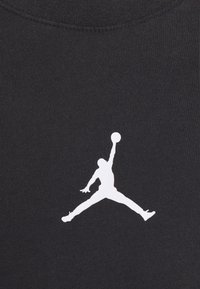 Czarna koszulka z gładką, bawełnianą fakturą, z białym logo Jumpman w dynamicznej pozie na piersi.