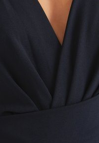 Navy Wickelkleid mit tiefem V-Ausschnitt, weichem Textilgewebe und gerafftem Detail an der Taille für eine schmeichelhafte Silhouette.