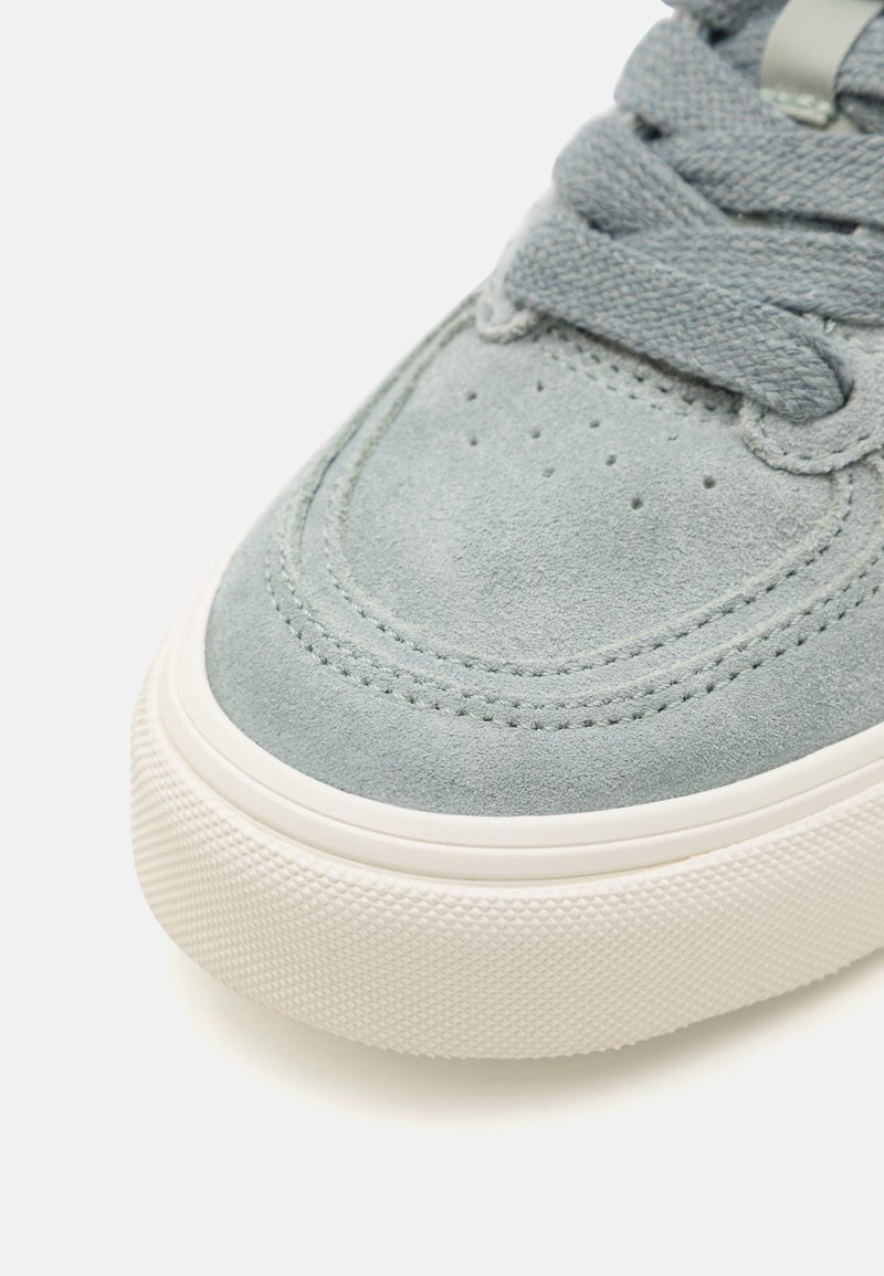 Sneaker grigia in suede con superficie texturizzata, punta rotonda, lacci piatti e suola in gomma bianca con un motivo a diamante.