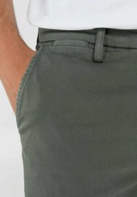 Pantalon en coton vert olive avec une texture lisse, comportant une poche latérale et une ceinture visible avec des passants.