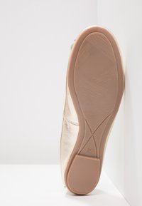 Gouden metalen platte schoen met een glad bovenwerk en een lichtbruine rubberen zool met textuurpatronen voor grip. Maat 37 staat op de zool vermeld.