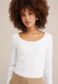 Top blanco de manga larga con acabo acanalado y escote amplio, combinado con pantalones beige. Textura suave y diseño ajustado en el torso.