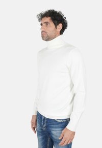 Maglione a collo alto bianco aderente, realizzato in materiale morbido con dettagli a coste sul colletto e sui polsini, abbinato a jeans blu.
