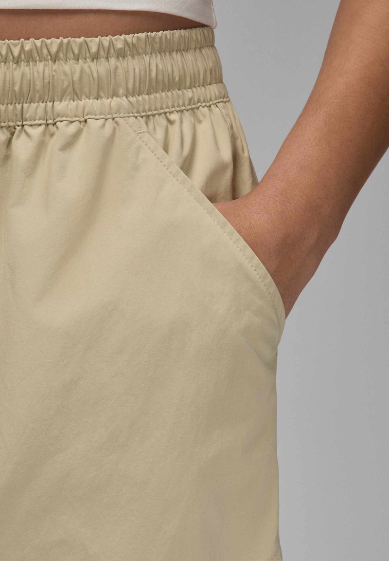 Shorts beiges légers avec une taille élastique et des poches latérales. Texture lisse avec un léger éclat et détails en tissu froncé.