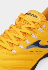 Φωτεινό κίτρινο αθλητικό παπούτσι με μαύρο λογότυπο, κίτρινες κορδόνια, γλώσσα από δίχτυ και λεπτομέρειες συστήματος εξαερισμού.