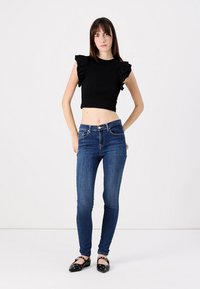 Black cropped top with ruffled sleeves, paired with dark blue skinny jeans and black flats featuring studded accents. Simple, fitted design.