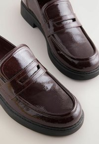 Mocassini in pelle patinata bordeaux con finitura testurizzata, caratterizzati da un dettaglio a fascia rialzato e una suola in gomma nera. Forma e design classici.
