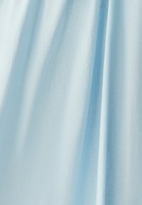 Šviesiai mėlynos spalvos audinys, turintis minkštą ir struktūruotą paviršių, pasižymintis švelniais klostėmis ir raukšlėmis, rodančiomis, kad medžiaga yra lengva ir orui pralaidi.