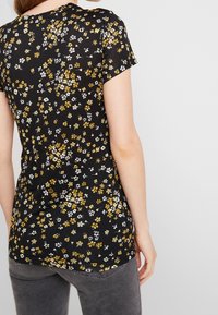 Camisa negra de manga corta con un estampado floral en blanco y amarillo. Tejido suave, diseño ajustado, dobladillo redondeado y cuello redondo.