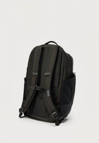 Μαύρο σακίδιο με επενδυμένους ιμάντες ώμου, ρυθμιζόμενο κούμπωμα στο στήθος, πλαϊνές θήκες και λαβή μεταφοράς σε απλό φόντο.