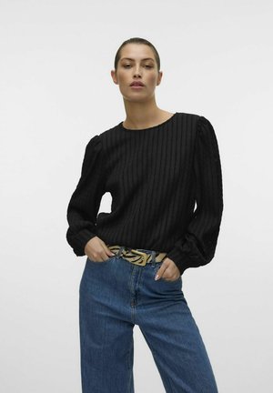 Schwarzes, geripptes Langarmshirt mit rundem Ausschnitt, kombiniert mit blauen, hochgeschnittenen Jeans und einem beigen, gemusterten Gürtel.