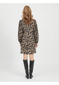 Vestido de manga corta con estampado de leopardo en tonos marrones y negros, con cintura ajustada y falda acampanada, combinado con botas negras hasta la rodilla.