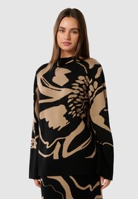 Maglione a maniche lunghe nera e beige con un motivo, realizzato in tessuto morbido. Presenta un disegno floreale astratto e una vestibilità rilassata.