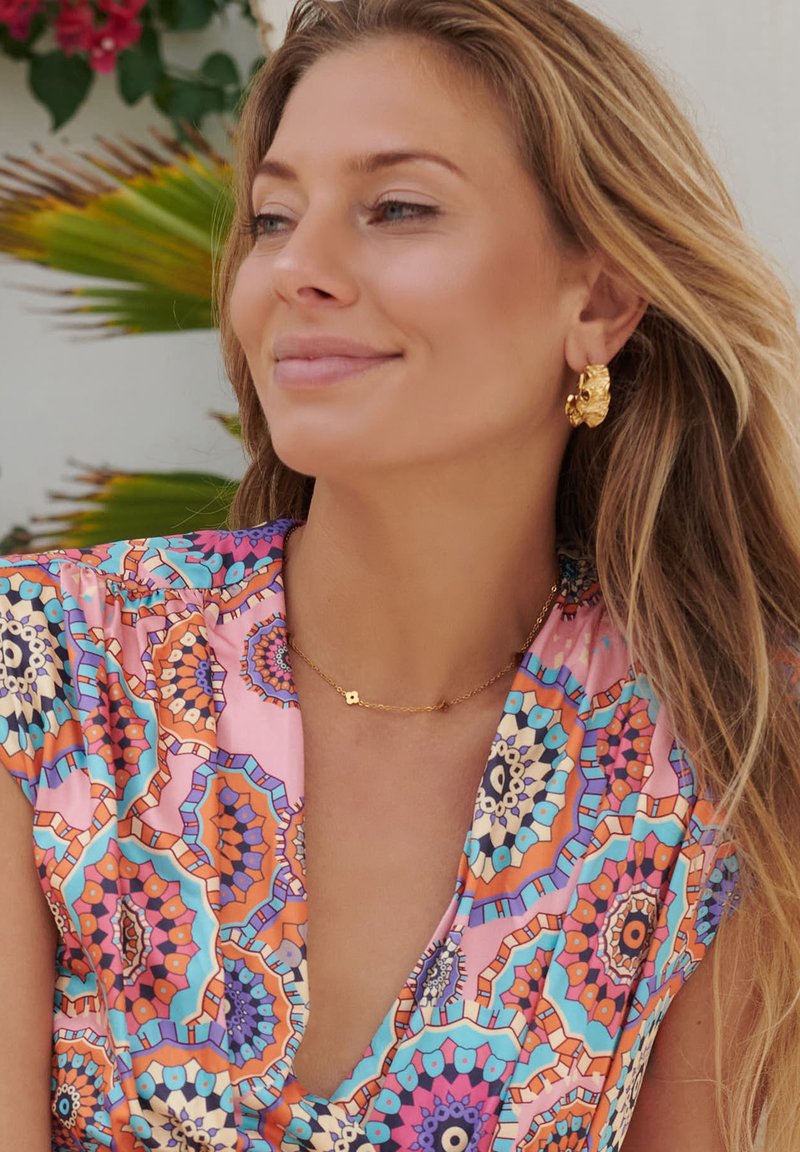 Colorful patterned dress featuring shades of pink, blue, and orange, paired with textured gold earrings and a delicate gold necklace.