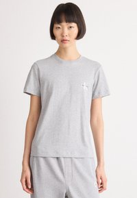 Pilkas medvilnės marškinėliai su trumpomis rankovėmis, apvaliu iškirpimu ir mažu baltu Calvin Klein logotipu ant krūtinės. Minimalistinis dizainas ir laisvas fasonas.