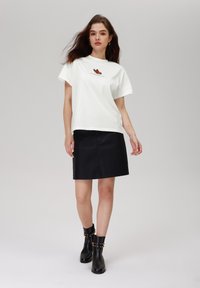 White cotton T-shirt with graphic design, paired with a black leather mini skirt and black ankle boots featuring decorative studs.