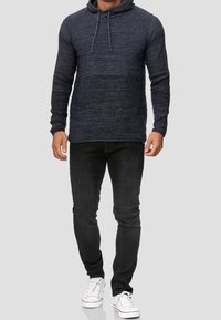 Marinblå stickad hoodie med en strukturerad yta, känguruficka och justerbara dragsnören, tillsammans med svarta slim-fit jeans och vita sneakers.