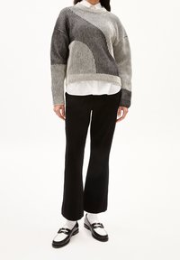 Gebreide trui met een geribbelde textuur in grijs en gebroken wit, met een asymmetrisch ontwerp. Gecombineerd met zwarte wijde broek en loafers.