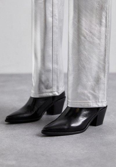 Zwarte leren enkellaarzen met een spitse neus en blokhak, gecombineerd met glanzende zilveren broeken, die slanke texturen en contrasterende kleuren laten zien.