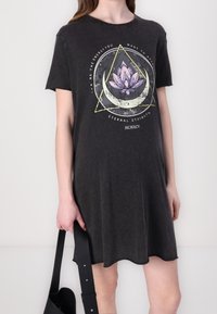 Robe t-shirt noire à coupe décontractée, ornée d'un design graphique d'une fleur de lotus et de formes géométriques dans des couleurs douces, à manches courtes.
