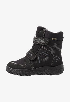Sort vinterstøvle til børn med to velcrobånd, Gore-Tex-mærkat, mønstret sål og forstærkede syninger til udendørs brug.