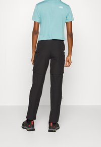 Svarta cargobyxor med dragkedjefickor, kombinerade med en ljusblå kortärmad skjorta. Stylad med svarta skor med röda accenter.