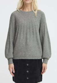 Maglione grigio lavorato a maglia con motivi a treccia, scollo rotondo e maniche a palloncino. Abbinato a una gonna in corduroy nera con bottoni.