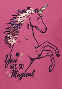 Roze T-shirt met een eenhoornontwerp, voorzien van een pailletten meerkleuren manen, zwarte contouren, en de tekst "Je bent zo magisch", met ster accenten.
