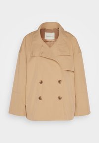 Beżowa podwójnie zapięta kurtka z szerokim kołnierzem, długimi rękawami i dużymi guzikami. Wykonana z gładkiego, sztywnego materiału.