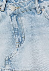 Světle modré džíny z denimu na detailním záběru, zobrazující přední kapsu, knoflík, poutko na opasek a kontrastní prošívání.