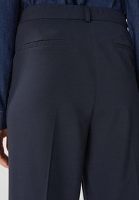 Marinblå byxor i texturerad tyg, med en åtsittande midja och två bakfickor, samt en ren, skräddarsydd silhuett.