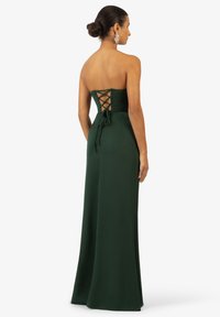 Abito da sera verde in satin senza spalline, con corpino aderente, dettaglio con lacci sulla schiena e gonna fluente lunga fino al pavimento.