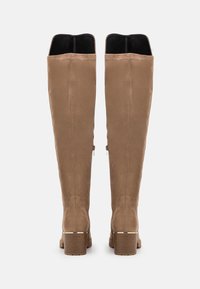 Botas de ante sintético en color beige hasta la rodilla, con un forro negro, un borde curvado, dos cremalleras laterales y un tacón apilado marrón.