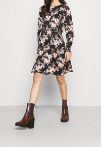 Black dress with pink floral pattern, long sleeves, cinched waist, and a flared skirt. Worn with brown heeled ankle boots.