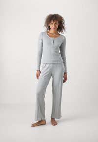 Ensemble de pyjama gris comprenant des manches longues, un col rond avec des boutons, et des bords effilochés aussi bien sur le haut que sur le pantalon. Texture ribbed douce sur l'ensemble.