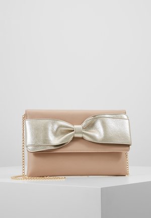 Borsa clutch beige con grande fiocco metallico dorato sul davanti e tracolla a catena dorata, mostrata su superficie bianca.