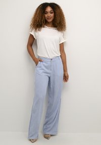 Top bianco con dettaglio in pizzo nel collo, abbinato a pantaloni larghi a righe blu e bianche, dotati di chiusura con bottone e tasche anteriori.