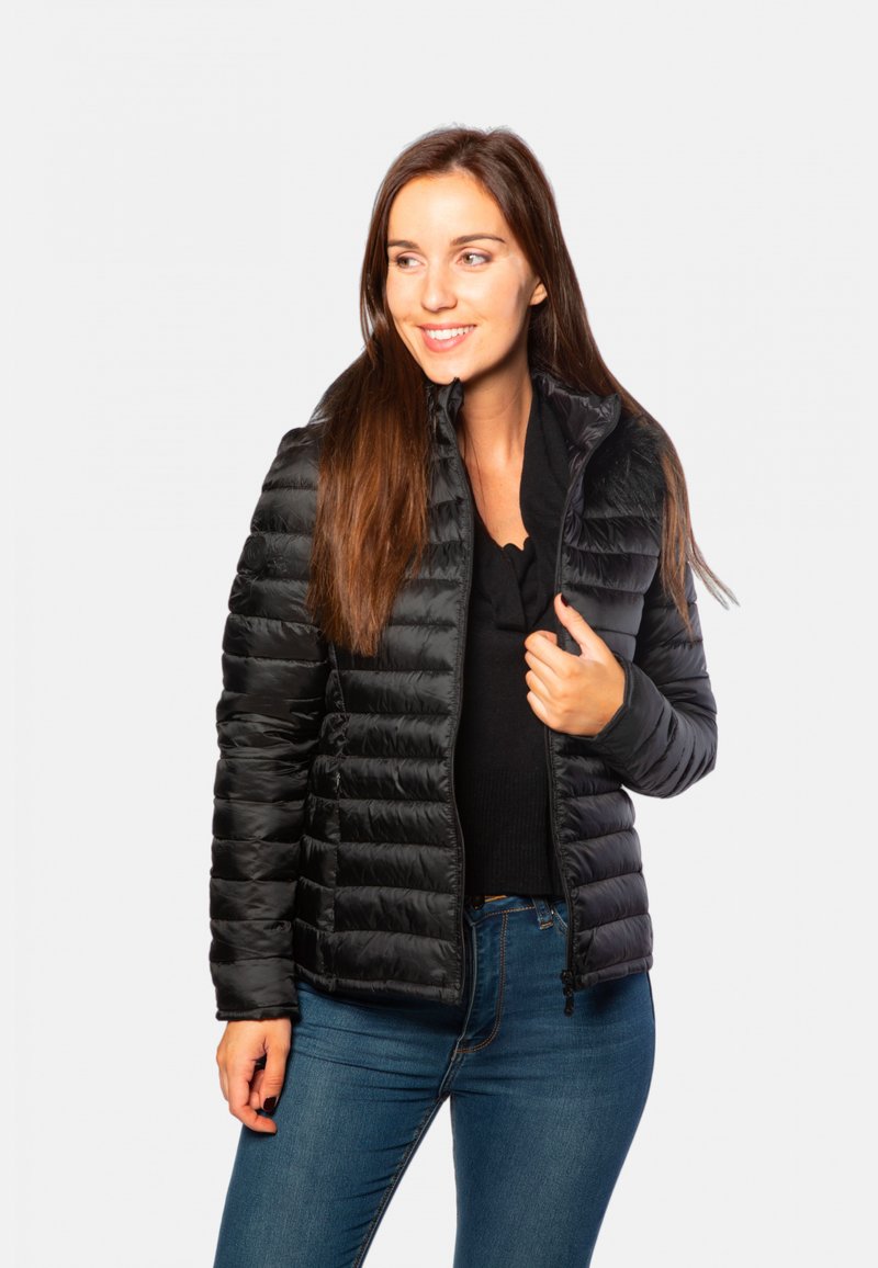 Doudoune noire avec fermeture zippée, texture matelassée et col montant, associée à un haut sombre et un jean bleu.
