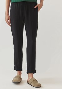 Schwarze, leichte Hose mit lässigem Schnitt, ausgestattet mit zwei vorderen Taschen, einem elastischen Bund und umgeschlagenen Säumen. Kombiniert mit beigen Slippern.
