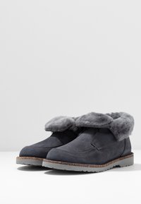 Mørkegrå suedes anklerstøvler med en blød grå pelskant, gummisål og en struktureret overflade. Har et simpelt slip-on design.