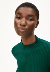 Groene geribbelde trui met een hoge halslijn en textuurstof, met een aangesloten ontwerp en minimalistische esthetiek.