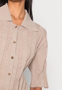 Chemise col bateau marron clair avec des côtes verticales, manches courtes et boutons marron ; tissu doux avec une finition texturée.