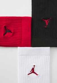 Tri parovi rebrastih crew čarapa: crne s crvenim logotipom, crvene sa crnim logotipom, i bijele s crvenim logotipom; s izvezenim Jumpman dizajnom.