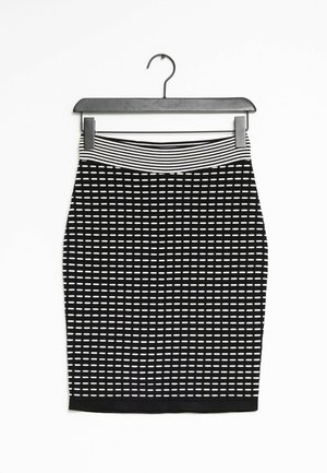 Jupe crayon noire avec motif de traits horizontaux blancs et ceinture élastique à rayures, suspendue sur un cintre noir sur fond blanc.