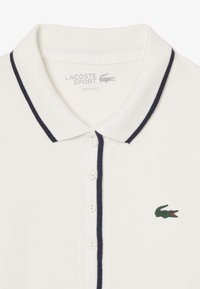 Vit polo som har mörknavy krage och knappslå. Har en broderad grön krokodil-logotyp på vänster bröst. Design med regular fit.