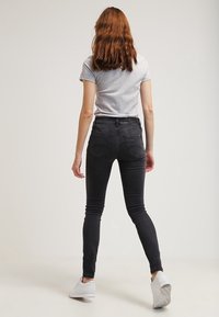 Höga svarta jeans i denim, med en figursydd design, bakfickor och en slät yta. Matchas med en grå t-shirt och vita skor.
