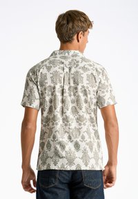 Camisa de manga corta en crema claro con un patrón floral verde; cuenta con un cuello con solapas y un dobladillo recto, fabricada en tela suave.
